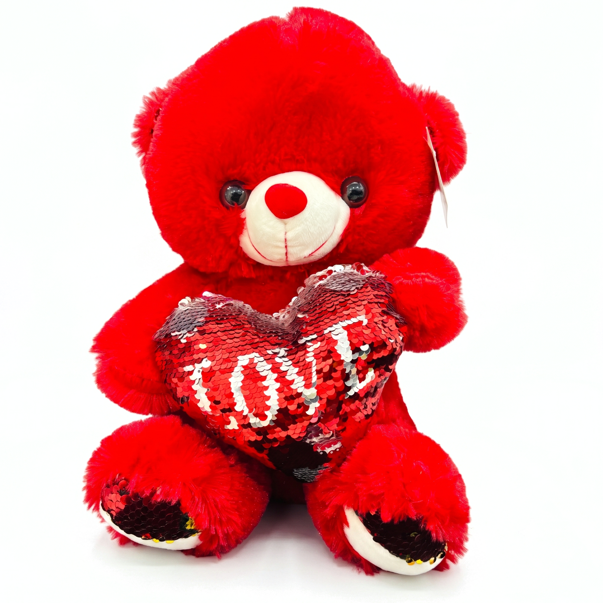 A red plush teddy bear holding a sequined heart-shaped pillow with the word 'LOVE' in white, photographed against a plain white background.