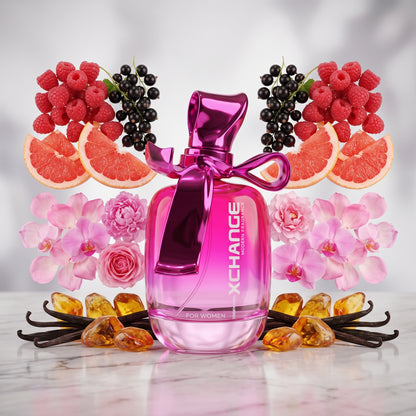 A pink perfume bottle labeled XCHANGE for Women, styled on a marble surface with raspberries, blackberries, grapefruit slices, pink flowers, vanilla beans, and amber gemstones around it.